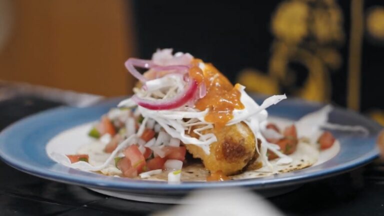A Plate of Fish Tacos with Crispy Fried Fish, Slaw, Pickled Onions, Pico De Gallo, and Spicy Sauce on A Charred Tortilla