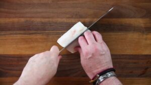 A Person Slicing a White Fish Fillet Into Portions on A Wooden Cutting Board