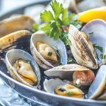 Close-up of a dish of steamed clams garnished with parsley and lemon slices
