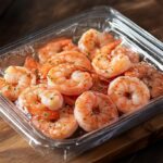 Seasoned cooked shrimp in a plastic container on a wooden board