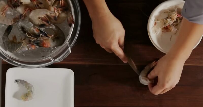 Hands deveining shrimp with a knife, showing how to devein shrimp
