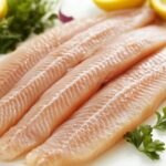 Four raw fish fillets arranged on a plate with lemon slices and parsley, illustrating the appearance of fresh seafood