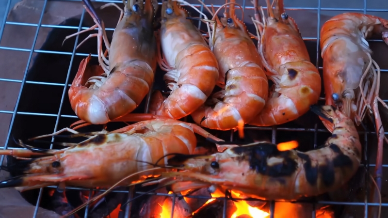 Grilled jumbo shrimp and prawns cooking over open flames on a metal grate