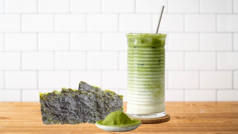 Crispy seaweed sheets are served beside a glass of unsweetened matcha latte with a spoon and a small dish of matcha powder