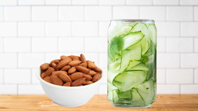 Roasted almonds in a bowl next to a glass of cucumber-mint water on a wooden surface