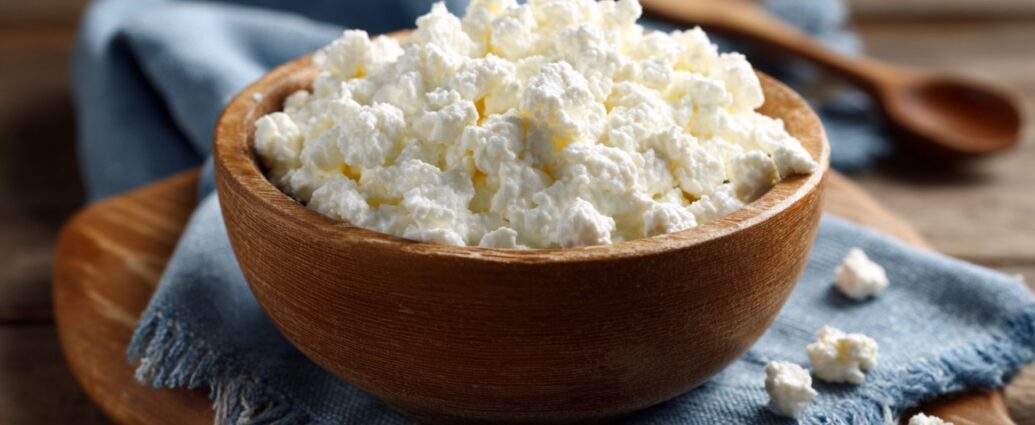 A wooden bowl filled with cottage cheese placed on a blue cloth napkin with a wooden spoon in the background