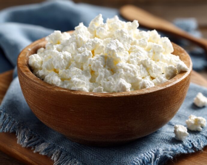 A wooden bowl filled with cottage cheese placed on a blue cloth napkin with a wooden spoon in the background