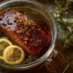 Glass jar with seasoned fish fillet, lemon slices, herbs, and brine for smoking