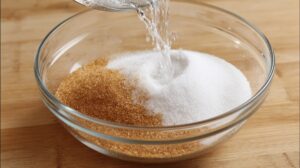 Close-up of water being poured into a bowl filled with white and brown sugar, preparing a brine mixture